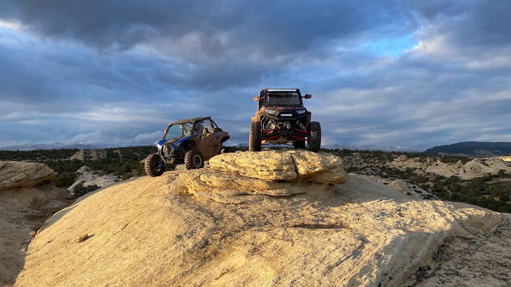 Side-by-side UTVs atop a large boulder with a desert view near Vernal Utah
