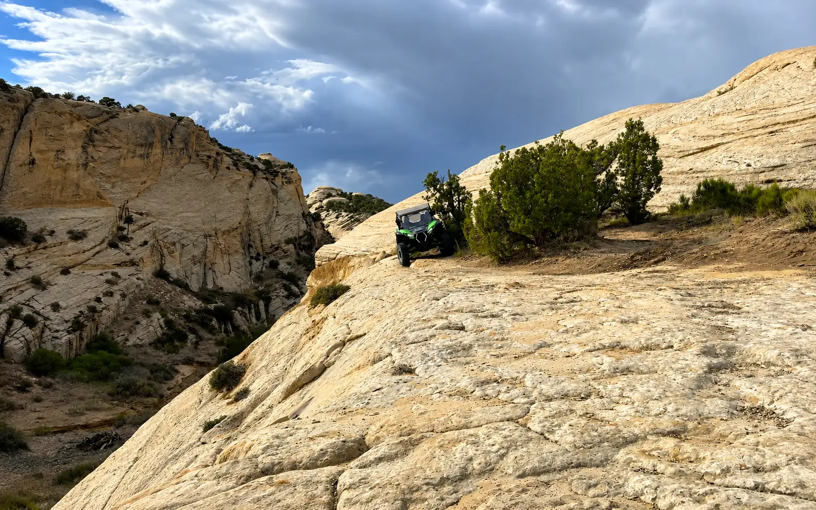 Side-by-side UTVs on slickrock under a stormy sky near Vernal Utah