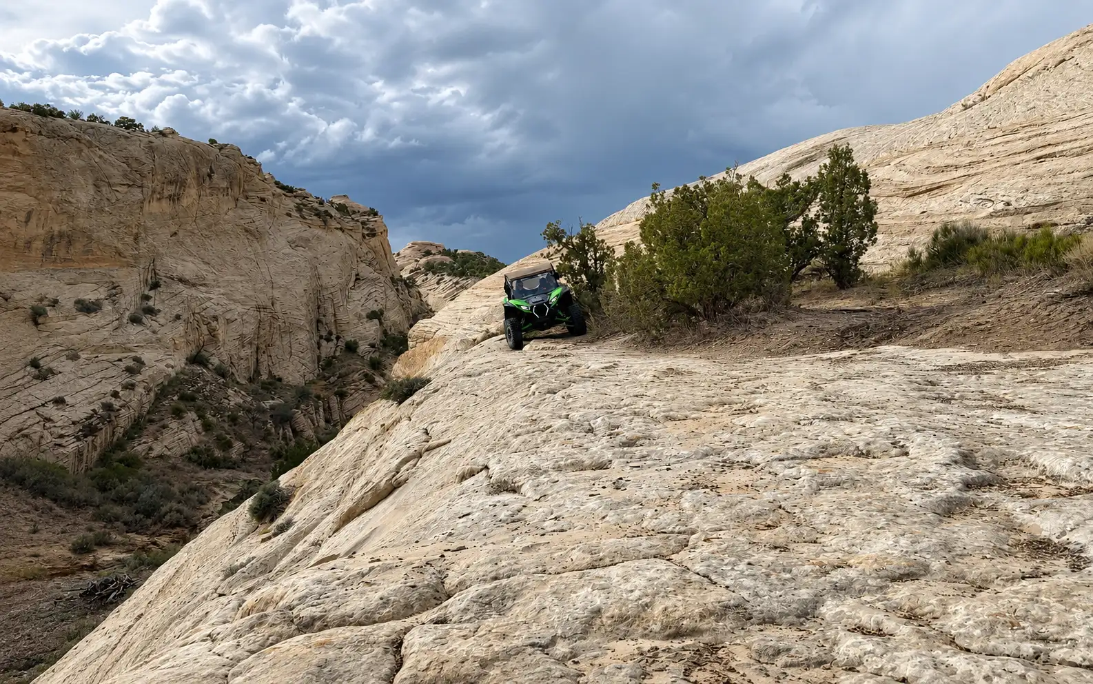 Side-by-side UTV on a slickrock climb under a stormy sky near Vernal Utah